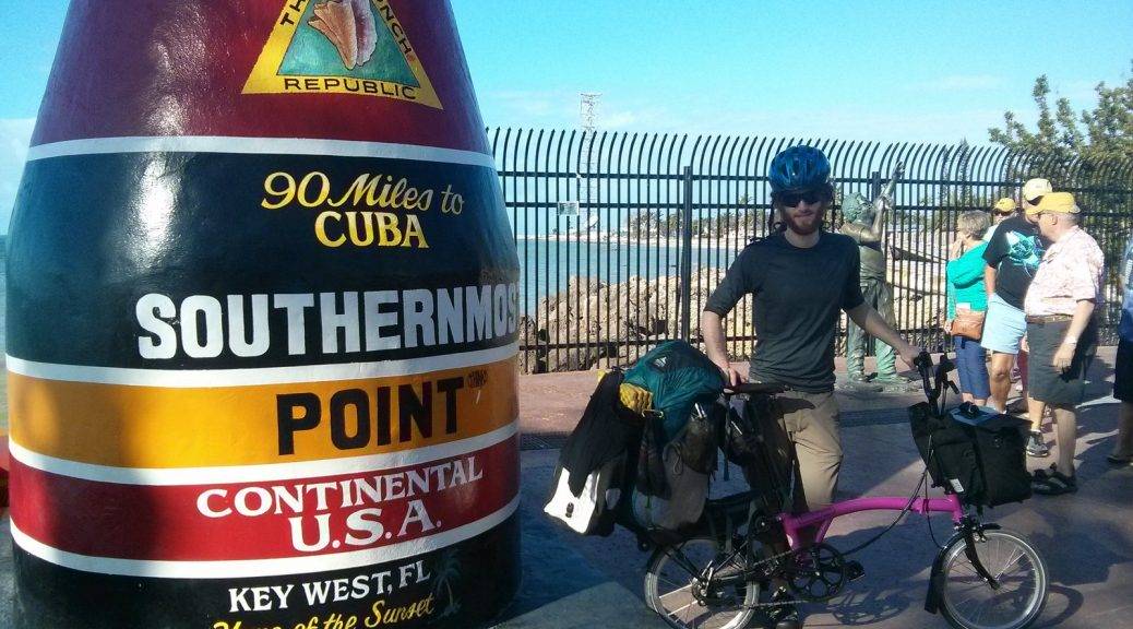 Mikey stands next to a giant monument that reads "The Conch Republic. 90 Miles to CUBA. SOUTHERNMOST POINT. CONTINENTAL USA. Key West, FL. Home of the Sunset."