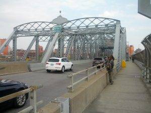 Mikey is standing in the walkway on a concrete-and-riveted-steel-truss bridge with a sign on it that reads "Madison Avenue Bridge"